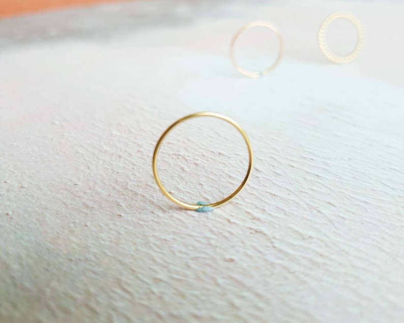 Puede incluir: Tres anillos de oro sobre una superficie blanca texturizada. El anillo del centro es un c&iacute;rculo simple, mientras que los dos anillos de la parte superior son texturizados.