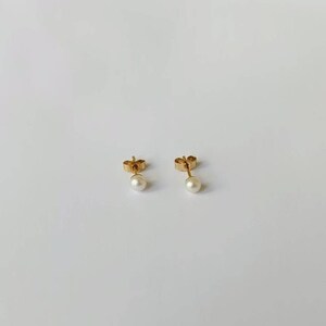 May include: A pair of gold stud earrings with small white pearl accents.