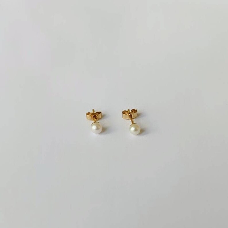 May include: A pair of gold stud earrings with small white pearl accents.