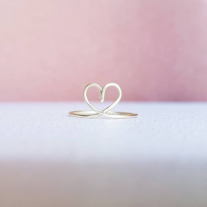 May include: A silver ring with a heart-shaped design. The ring is made of thin wire and has a delicate, minimalist look.