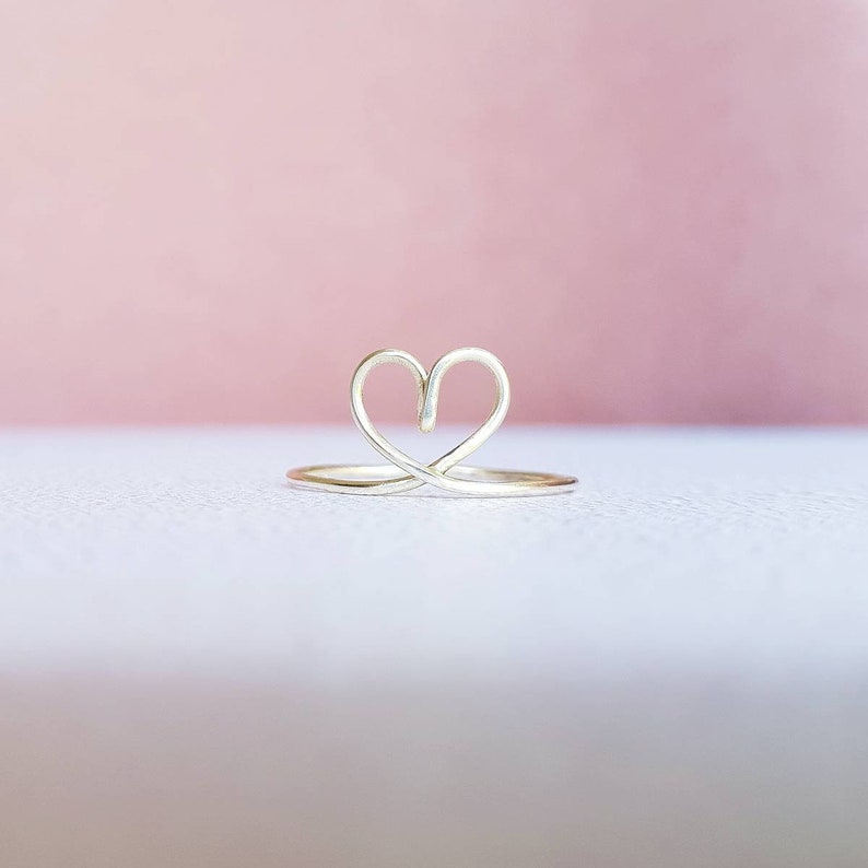 May include: A silver ring with a heart-shaped design. The ring is made of thin wire and has a delicate, minimalist look.