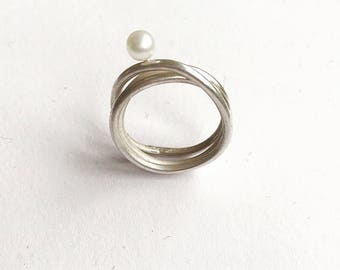 May include: A silver ring with a pearl on top. The ring is made of three intertwined bands.