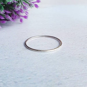 May include: A simple silver band ring, shown on a white wooden surface.