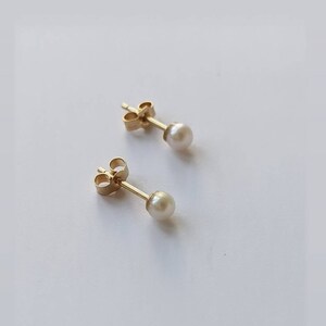 May include: A pair of gold pearl stud earrings. The earrings have a simple design with a small, round pearl set in a gold setting.