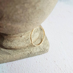 K&ouml;nnte beinhalten: Ein einfacher goldener Ring mit geh&auml;mmerter Textur. Der Ring liegt auf einer strukturierten, hellbraunen Oberfl&auml;che.