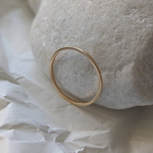 May include: A simple gold band ring, resting on a white rock.