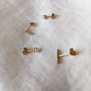 May include: Four gold earrings, two with small white pearls and two with a textured gold bar design.