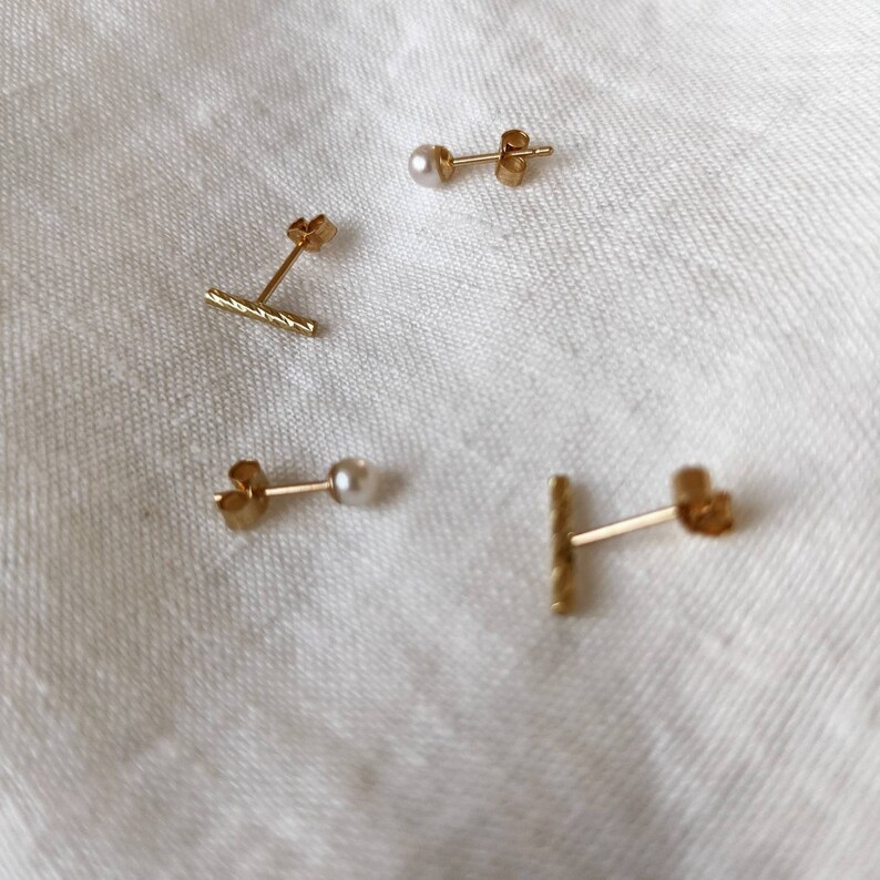 May include: Four gold earrings, two with small white pearls and two with a textured gold bar design.