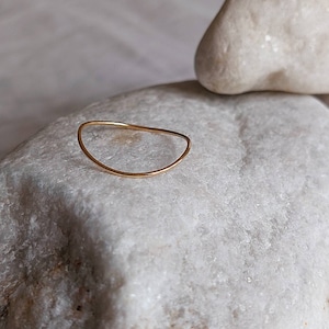 May include: A thin gold ring with a curved, crescent shape. The ring is sitting on a white rock.