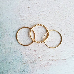 Puede incluir: Tres anillos de oro, uno con textura de cuentas, sobre un fondo blanco.