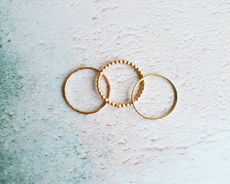 Puede incluir: Tres anillos de oro, uno con textura de cuentas, sobre un fondo blanco.