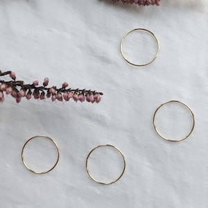 Puede incluir: Cuatro anillos minimalistas dorados sobre un fondo de tela blanca. Los anillos son simples y delicados, con forma circular.