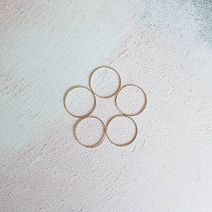 Puede incluir: Seis anillos de metal de color dorado dispuestos en un patr&oacute;n circular sobre un fondo blanco texturizado.