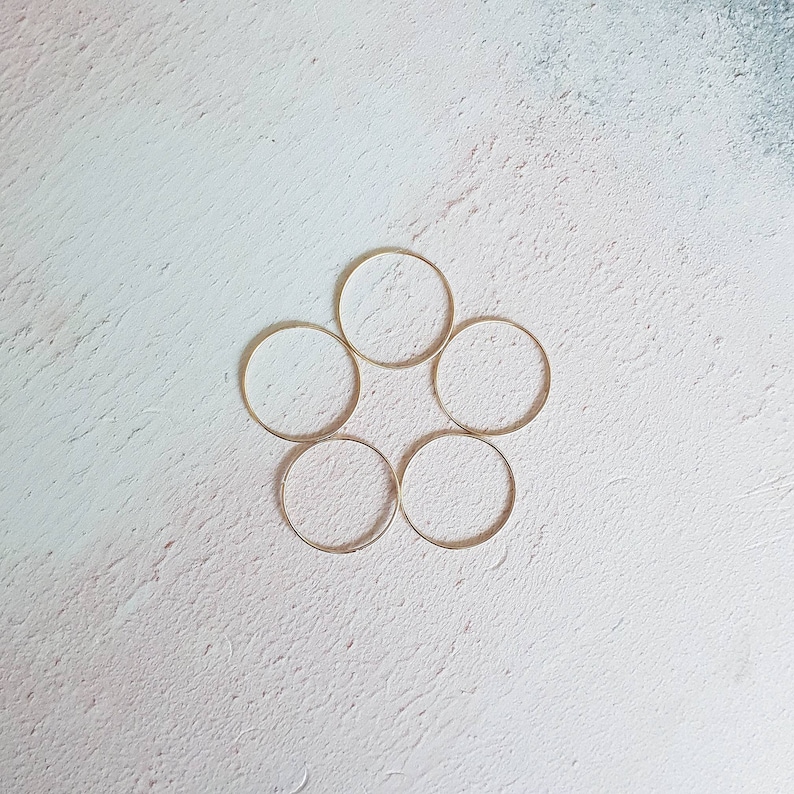 Puede incluir: Seis anillos de metal de color dorado dispuestos en un patr&oacute;n circular sobre un fondo blanco texturizado.