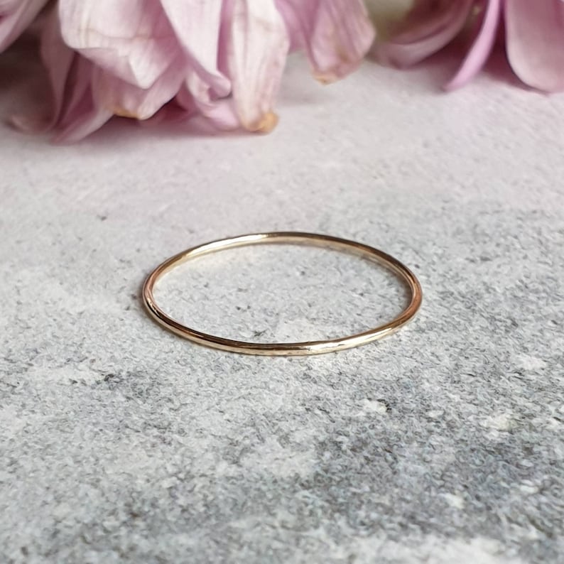 Puede incluir: Un anillo de banda de oro fino y simple. El anillo es liso y tiene un acabado pulido.