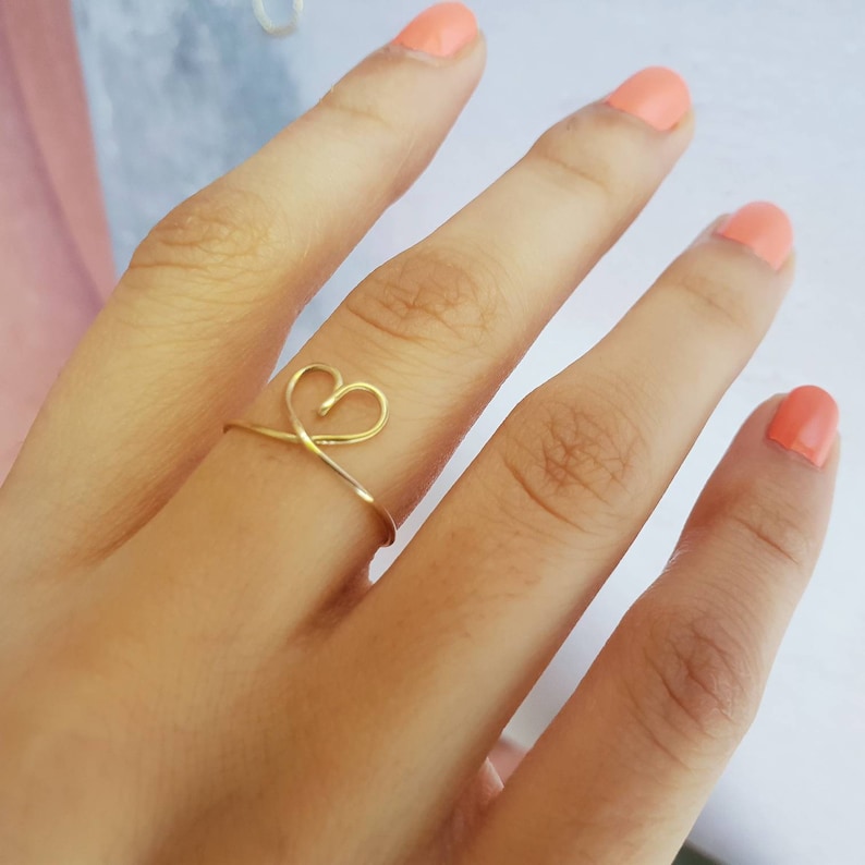 May include: A gold heart-shaped ring on a finger.