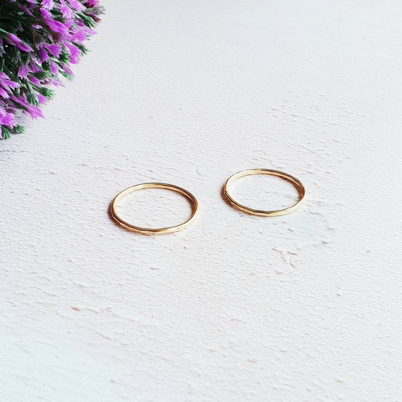 K&ouml;nnte beinhalten: Zwei d&uuml;nne goldene Ringe auf einer wei&szlig;en Oberfl&auml;che. Die Ringe sind schlicht und zart, mit einer geh&auml;mmerten Textur.
