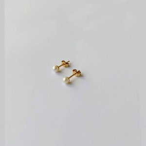 May include: A pair of gold stud earrings with small white pearl accents.