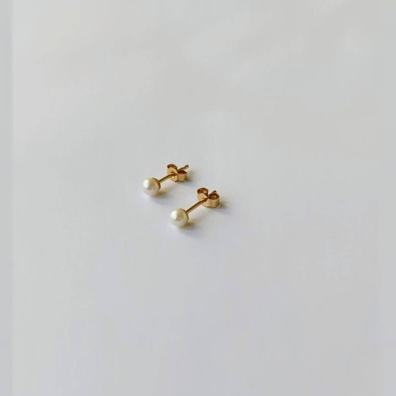 May include: A pair of gold stud earrings with small white pearl accents.