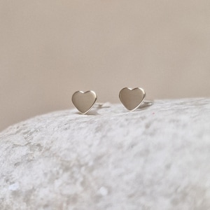 Puede incluir: Un par de pendientes de plata en forma de corazón. Los pendientes son pequeños y delicados, y son perfectos para el uso diario.