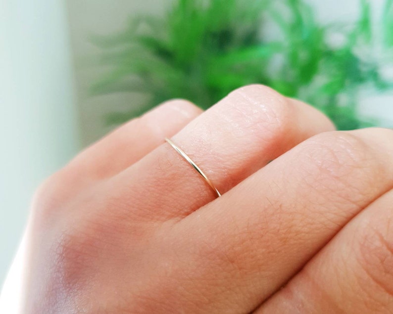 Puede incluir: Un anillo de banda de oro delgado usado en un dedo.