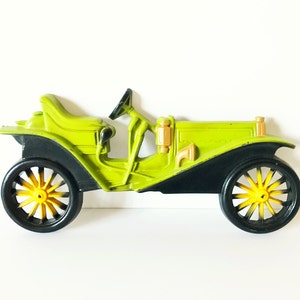 Puede incluir: Un coche de juguete vintage verde con ruedas negras y detalles amarillos. El coche tiene un dise&ntilde;o detallado y est&aacute; hecho de pl&aacute;stico.