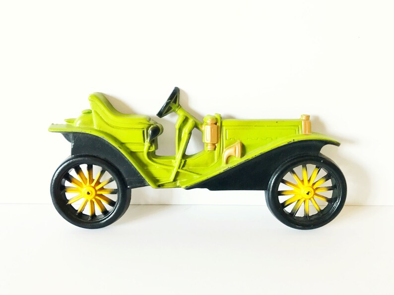 Puede incluir: Un coche de juguete vintage verde con ruedas negras y detalles amarillos. El coche tiene un dise&ntilde;o detallado y est&aacute; hecho de pl&aacute;stico.