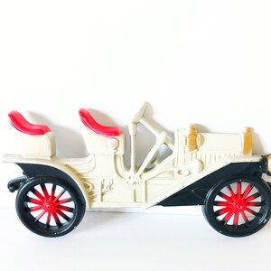 Puede incluir: Un coche de juguete vintage blanco y negro con asientos rojos. El coche tiene un dise&ntilde;o detallado y est&aacute; hecho de pl&aacute;stico.