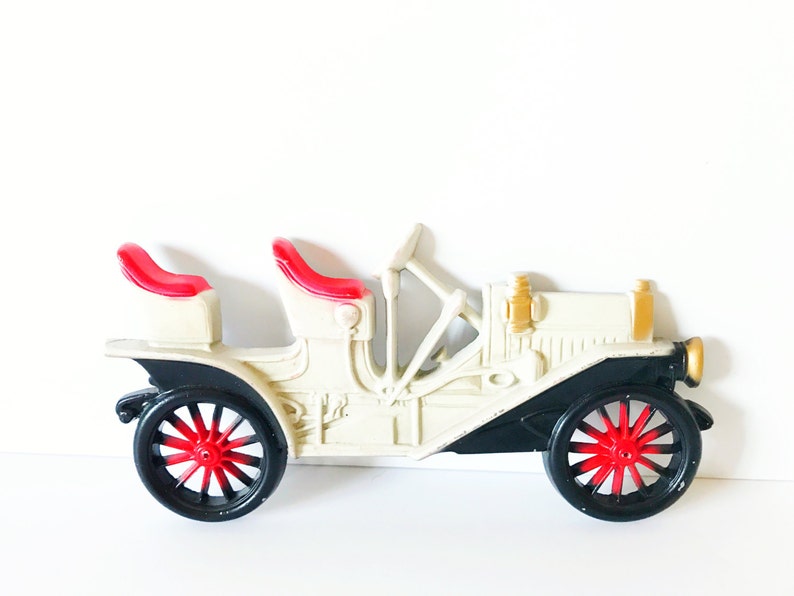 Puede incluir: Un coche de juguete vintage blanco y negro con asientos rojos. El coche tiene un dise&ntilde;o detallado y est&aacute; hecho de pl&aacute;stico.