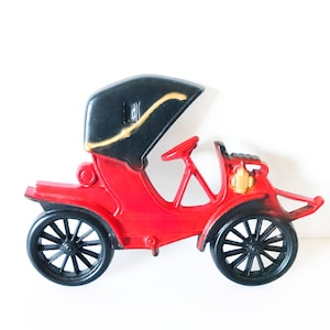 Puede incluir: Un coche de juguete rojo con techo negro y detalles dorados. El coche tiene un dise&ntilde;o detallado y est&aacute; hecho de pl&aacute;stico.