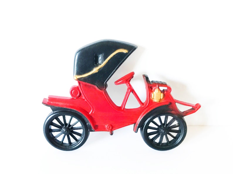 Puede incluir: Un coche de juguete rojo con techo negro y detalles dorados. El coche tiene un dise&ntilde;o detallado y est&aacute; hecho de pl&aacute;stico.