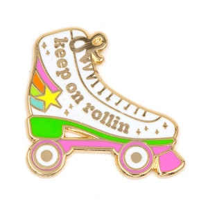 May include: Gold roller skate pin with a white base, green wheels, pink accents, and the text "keep on rollin'" in gold letters.