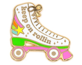 May include: Gold roller skate pin with a white base, green wheels, pink accents, and the text "keep on rollin'" in gold letters.
