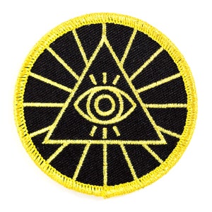 May include: A black and yellow embroidered patch with an all-seeing eye inside a triangle. The eye is surrounded by rays of light.
