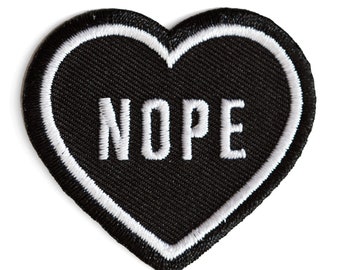 May include: Black heart-shaped patch with white stitching around the edges. The word "NOPE" is embroidered in white on the patch.