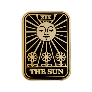May include: Gold-colored metal pin with a black background depicting the The Sun tarot card. The card features a sun with a face and three flowers.