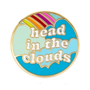 May include: Gold-colored pin with a blue, green, and white cloud design. The pin says "head in the clouds" in white letters with a gold outline.