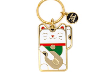 May include: A gold-coloured keyring with a white, gold, red, and green Maneki-neko cat design. The cat is waving its paw, and the keyring includes a small charm with the text "THESE ARE THINGS".