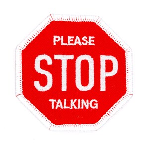 May include: Red octagonal stop sign with white stitching around the edges. The sign says "Please Stop Talking" in white text.