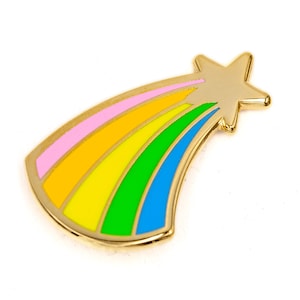 May include: A gold-colored metal pin shaped like a shooting star. The star is at the top, with a rainbow of colors trailing behind it: pink, orange, yellow, green, and blue. The pin has a shiny, smooth finish.