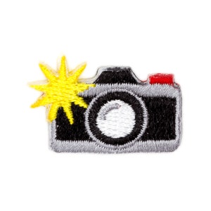 May include: A black and gray embroidered camera with a yellow flash. The camera has a white lens and a red top.