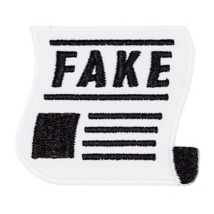 May include: White fabric patch with black embroidery of a newspaper headline that reads "FAKE".
