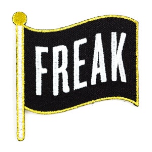 May include: Black fabric flag with a yellow border and a gold pole. The flag says "FREAK" in white letters.