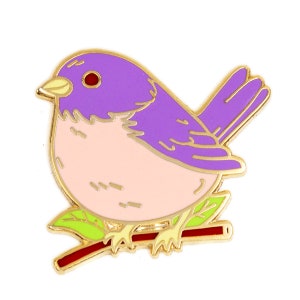 May include: A purple and pink enamel pin of a bird perched on a branch. The bird has a red eye and a yellow beak.