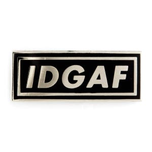 May include: A black and silver enamel pin with the text "IDGAF" in white letters.