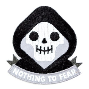 May include: Embroidered patch featuring a cartoon grim reaper skull in a black hood. The skull is white with black eye sockets and a stitched mouth. A gray banner below reads "NOTHING TO FEAR" in white letters. The patch has a white background.