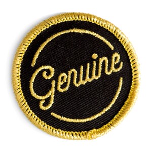 May include: A round, black fabric patch with a gold embroidered border and the word "Genuine" in gold thread.