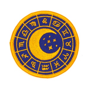 May include: A blue and yellow embroidered patch with a crescent moon and stars in the center. The outer circle features the astrological signs of the zodiac.