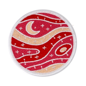 May include: A round, white-edged patch with a red and cream design. The design features wavy lines and a crescent moon with white stars.
