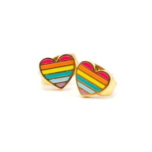 May include: A pair of gold heart-shaped earrings with a rainbow stripe design. The stripes are pink, yellow, orange, blue, and purple.